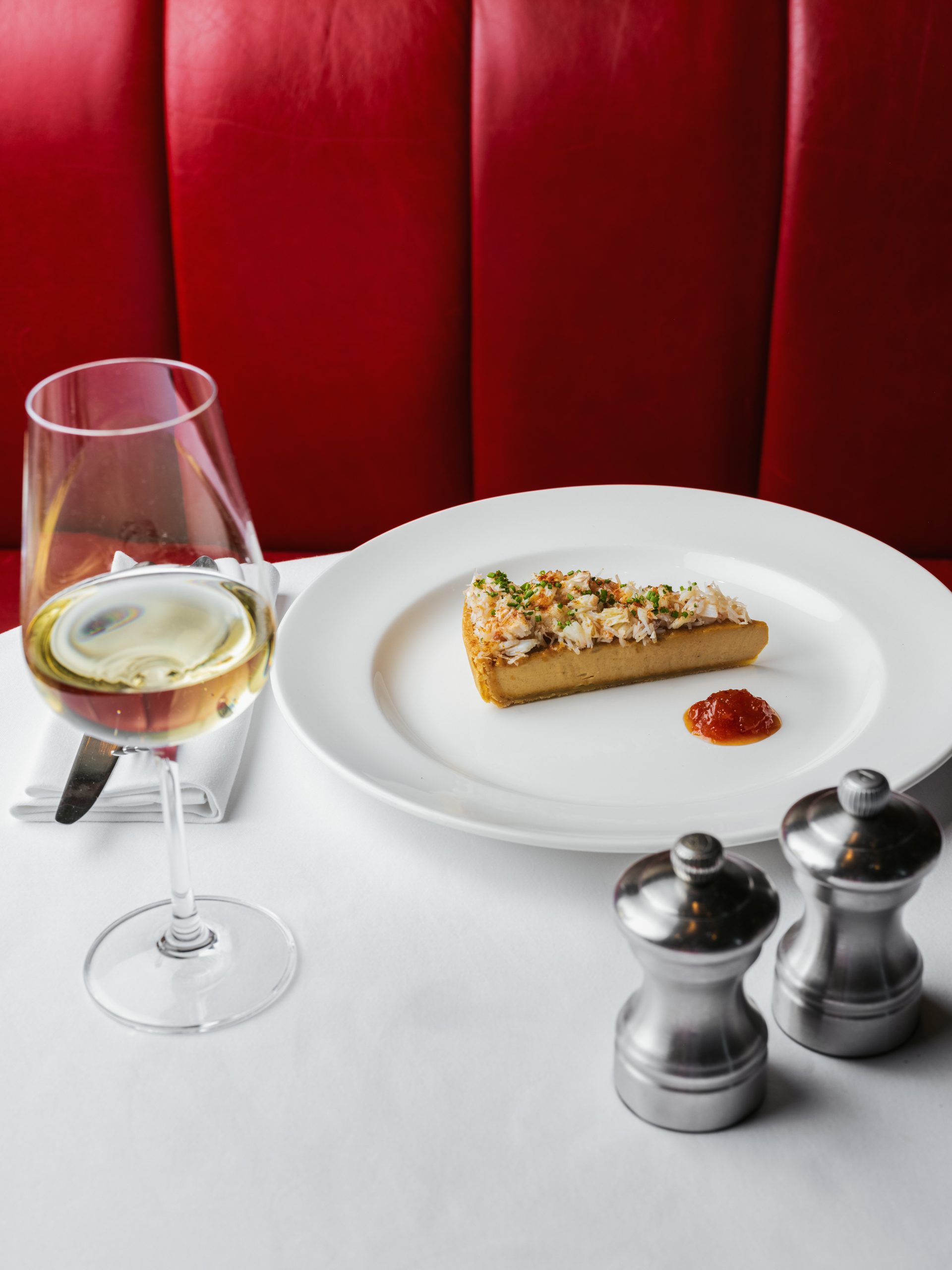 Crab tart with white wine glass and silver condiments on white tablecloth table at Bistrot at Wild Honey St James's London